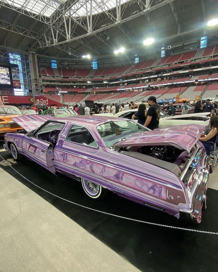 an old purple car is parked in the middle of a showroom with people looking at it