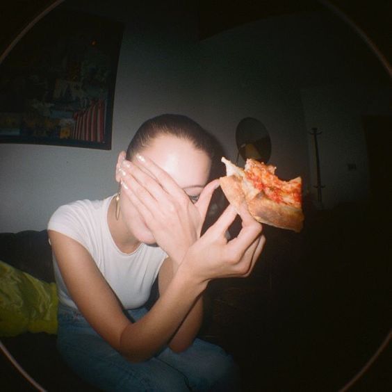 a woman covering her eyes while eating a slice of pizza in front of her face