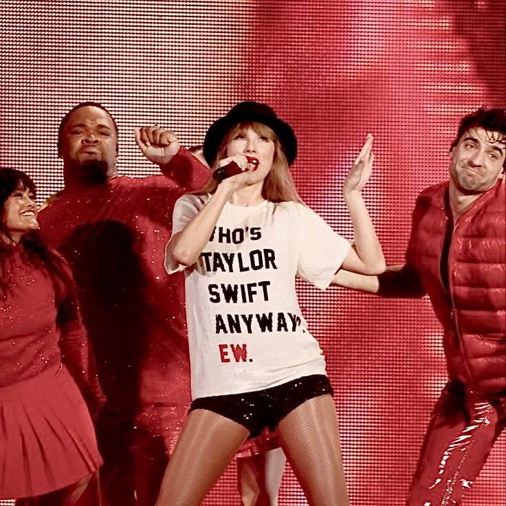 taylor swift performing on stage with other dancers behind her and the singer holding a microphone