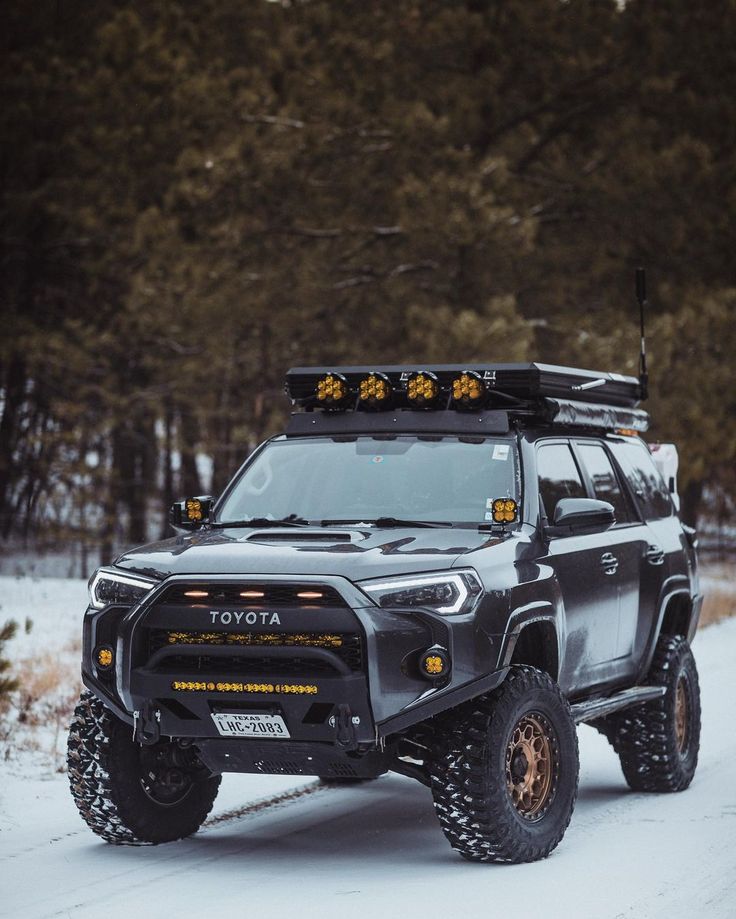 an suv is driving through the snow with its lights on and no roof rack attached to it