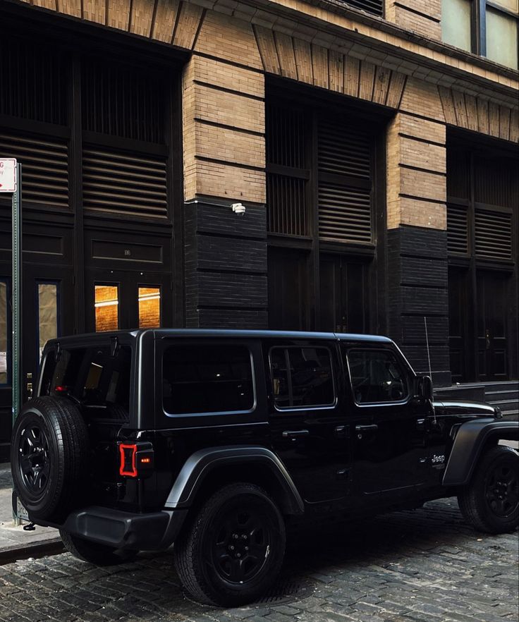 a black jeep parked in front of a tall building on a city street next to a sidewalk