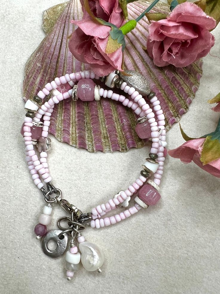 Sweet triple strand of small light pink glass beads from Ghana. Each strand has different accents. The bracelet is sized for a 7 inch wrist with extra links for size adjustment. One strand has faceted pyrite rondelle which border bone beads with silver tone domed caps. The new stand features silver ones flower connectors, Czech flowers, bone rings. And the last strand features pink glass crow beads with bone rings. All are strung on flexible wire. A lobster clasp with extra rings adorns the clasp. Several beaded charms, a freshwater pearl and a silver toned charm hang from the clasp area. One of a kind. All of my pieces are created with great care, quality elements and attention to detail. I hope you are happy with your purchase and should you have any concerns or questions, please let me Handmade Pink Beaded Strand Bracelets, Pink Rondelle Beaded Bracelets, Adjustable Double Strand Bracelets With Faceted Beads, Silver Double Strand Beaded Bracelet, Adjustable Double Strand Beaded Bracelet With Faceted Beads, Adjustable Double Strand Beaded Jewelry, Adjustable Double Strand Bracelet With Faceted Beads, Silver Double Strand Beaded Bracelets With Gemstones, Pink Silver Beaded Bracelet