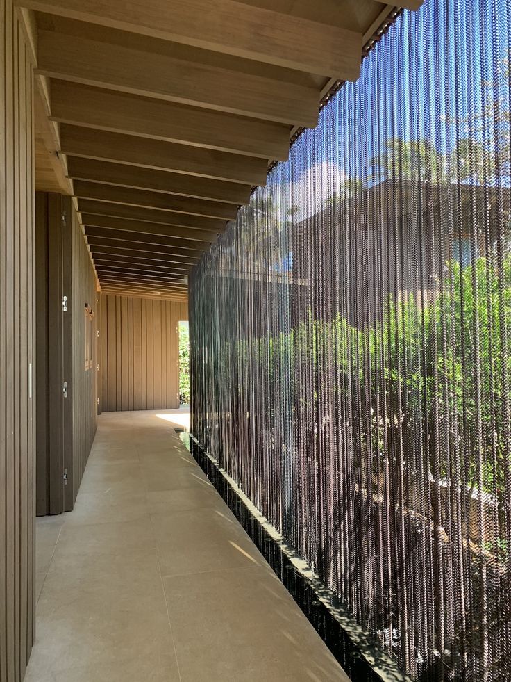 a long hallway with metal slats on the wall and trees in the background,