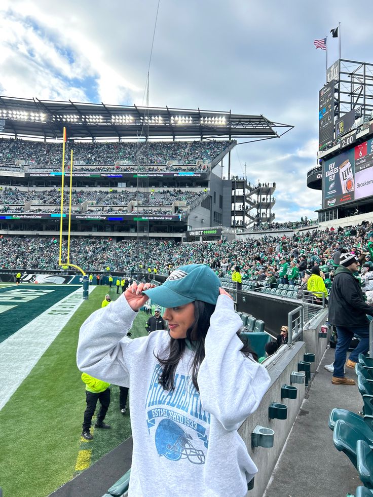 a woman wearing a hat standing in the stands at a football stadium with her hands on her head