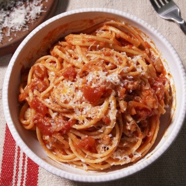 a white bowl filled with pasta and sauce on top of a table next to a fork