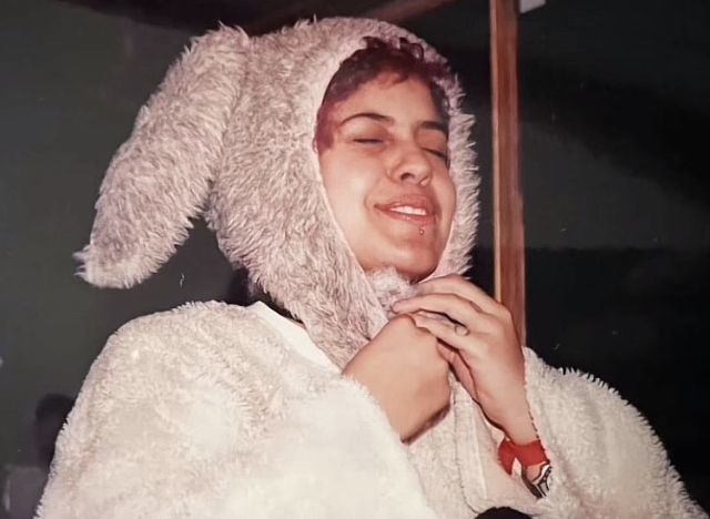 a woman wearing a bunny ears hat and fur coat with her hands under her chin