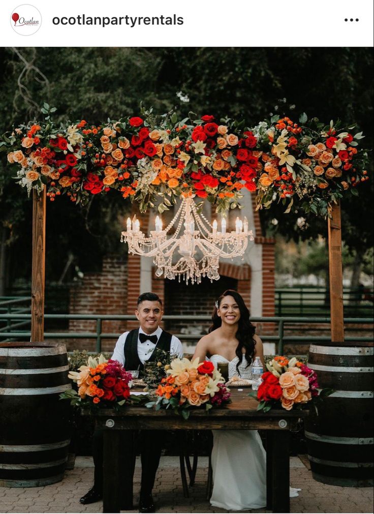 a man and woman sitting at a table in front of wine barrels with chandelier