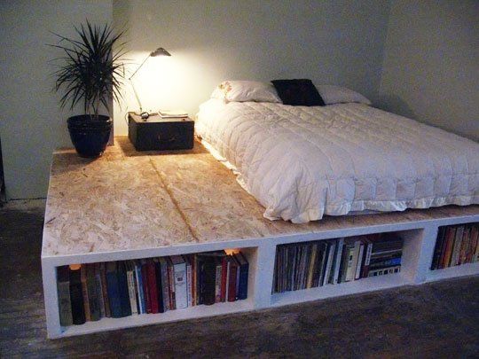 a bed sitting on top of a wooden platform with bookshelves underneath it and a plant in the corner