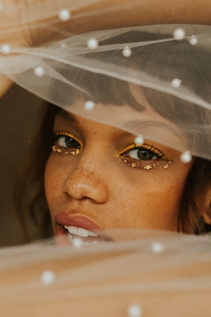 a close up of a woman wearing a veil and gold eyeshade with white dots on her face