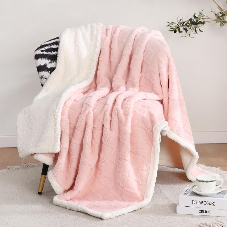 a pink and white blanket sitting on top of a chair next to a coffee cup