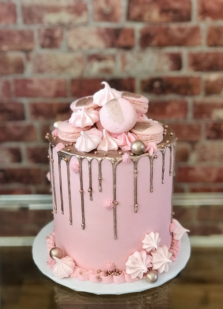 a pink cake with icing dripping down the side on a table next to a brick wall