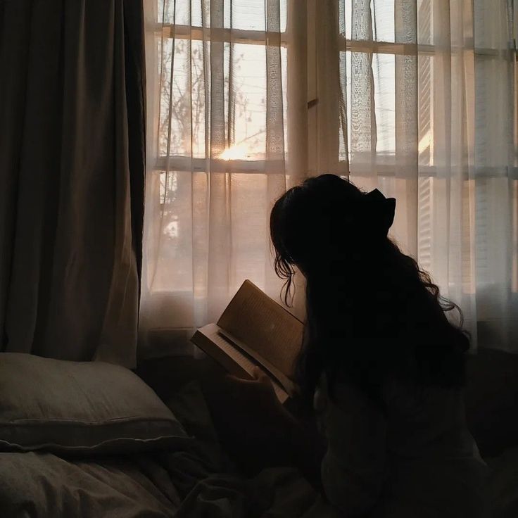 a woman sitting in front of a window reading a book