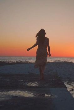 a woman walking on the beach at sunset with her arms out to the water and holding a baseball bat