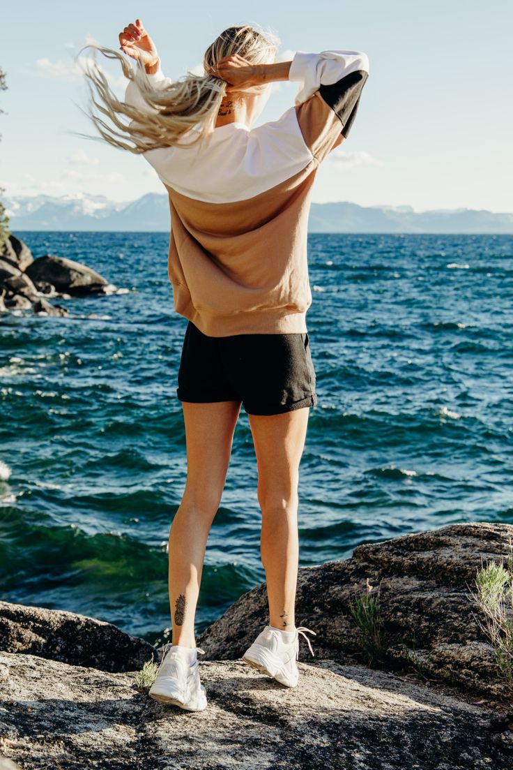 a woman standing on top of a rock next to the ocean with her hair blowing in the wind