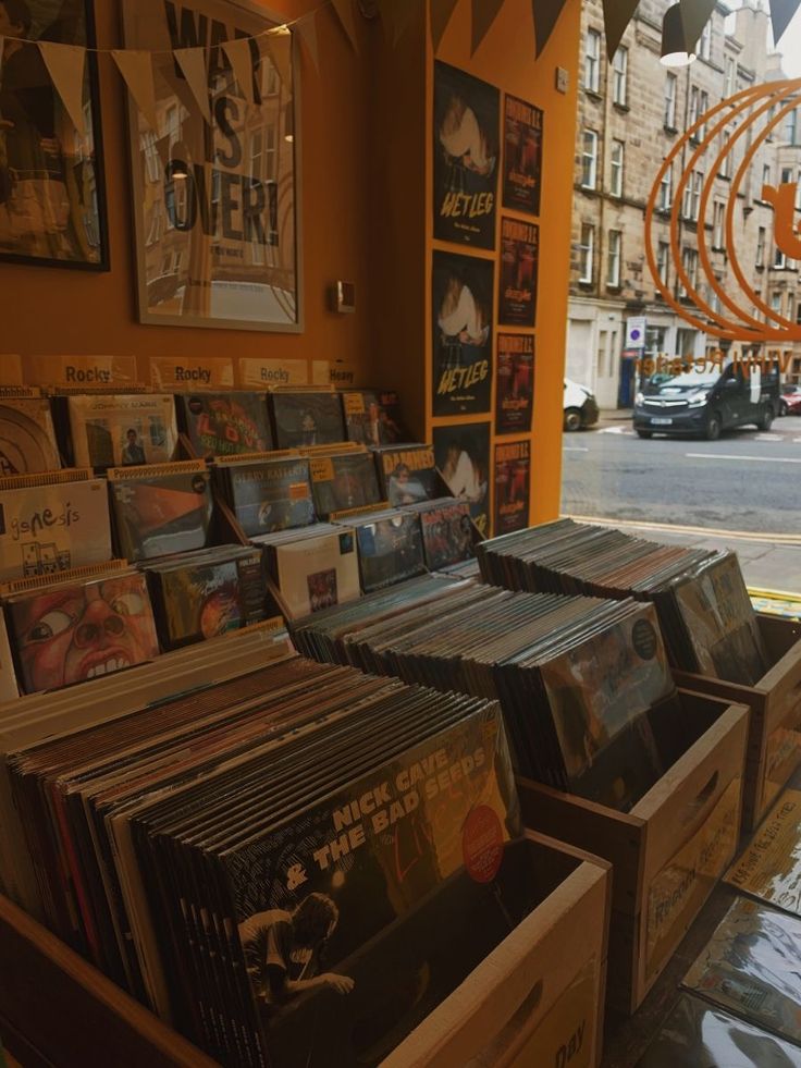 many records are on display in front of an orange wall with posters and pictures hanging from it