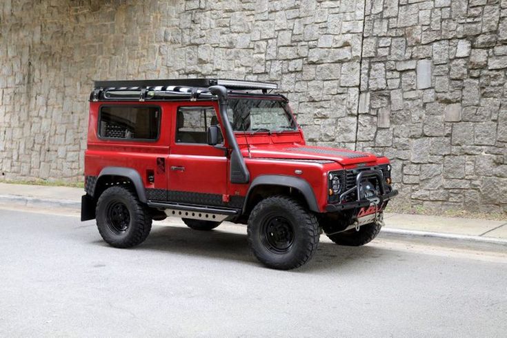 a red jeep parked in front of a stone wall