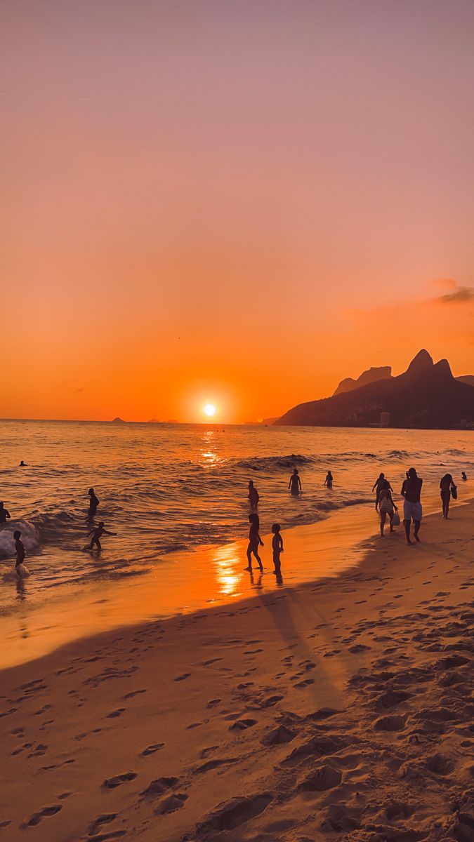 many people are walking on the beach at sunset