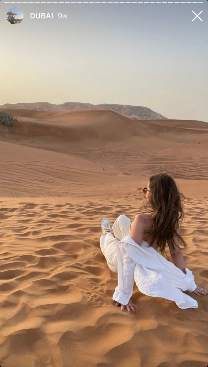 a woman sitting on top of a sandy beach next to a desert area with sand dunes