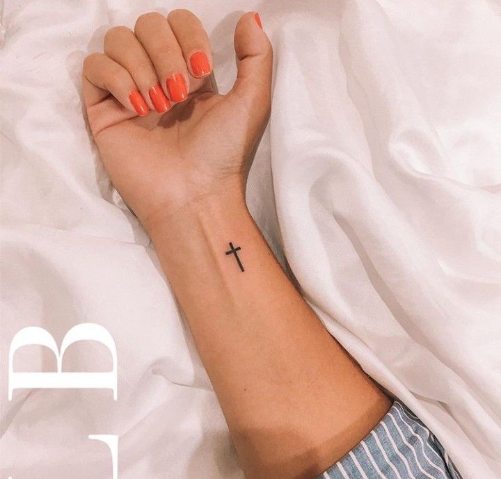 a woman's arm with a small cross tattoo on her left wrist and an orange manicure