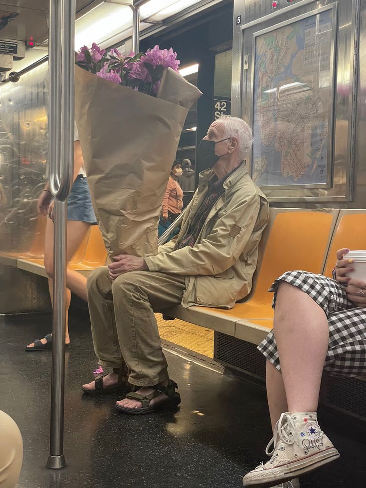 an old man sitting on a subway train with flowers in his bag