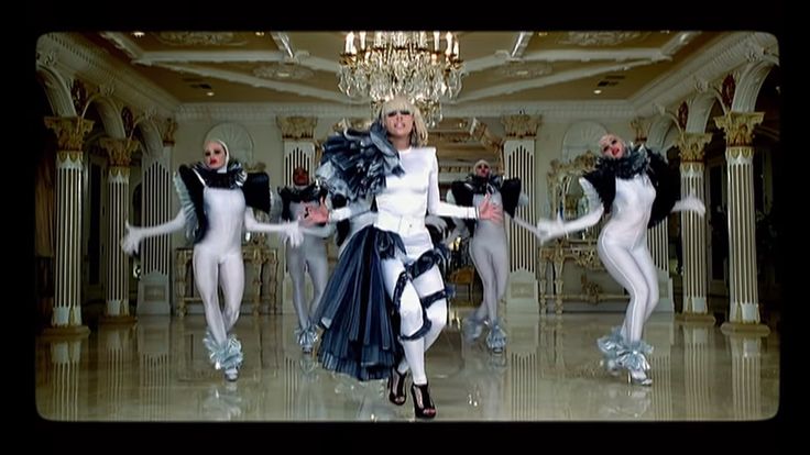 a group of women in white and black outfits dancing on a marble floor with chandeliers hanging from the ceiling