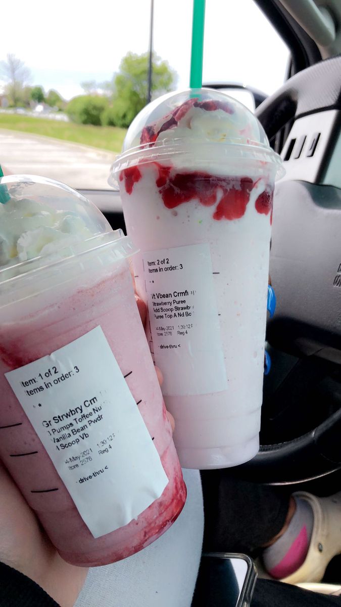 two drinks in plastic cups sitting next to each other on a car steering wheel seat