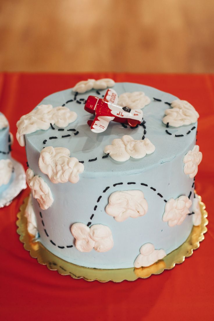 a blue cake with white clouds and a red plane on top is sitting on a table