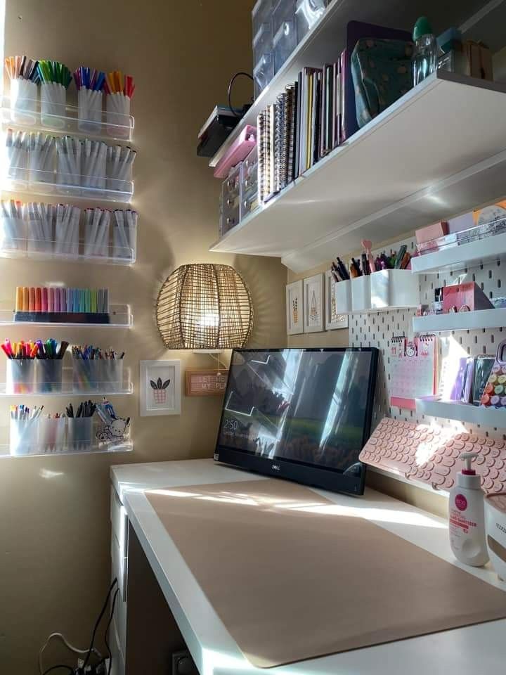 a desk with a computer monitor on top of it next to shelves filled with pens and pencils