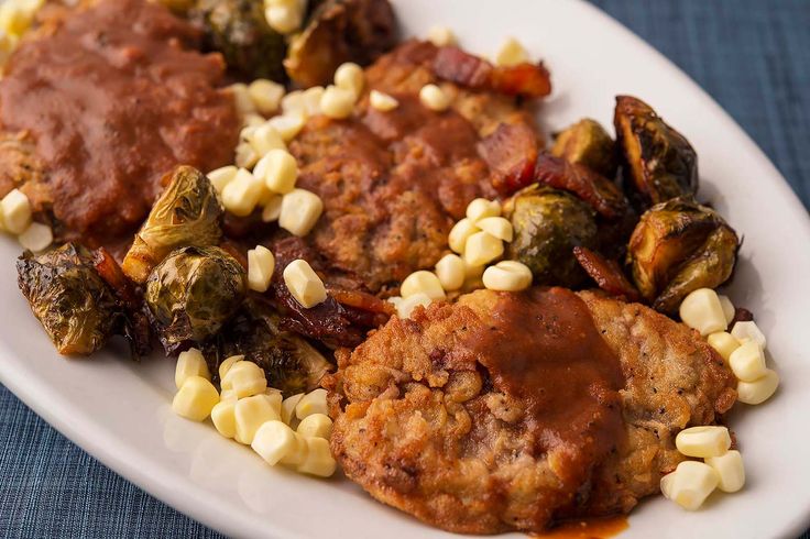 a white plate topped with meat and vegetables covered in gravy next to corn