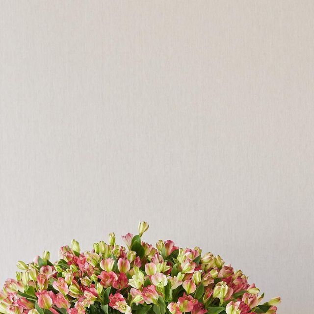 a vase filled with pink and white flowers on top of a wooden table next to a wall