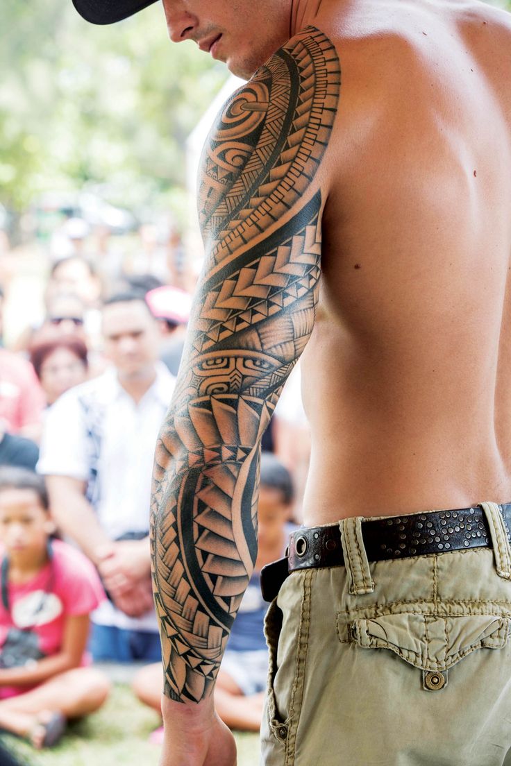 a man with a large tattoo on his arm and chest standing in front of an audience