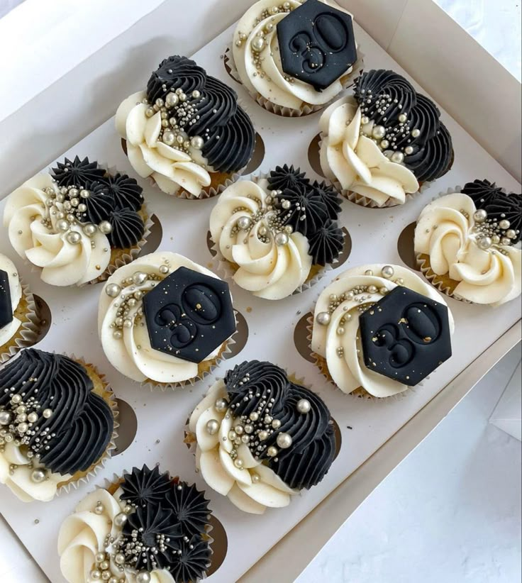 twelve decorated cupcakes in a box with black frosting and white icing