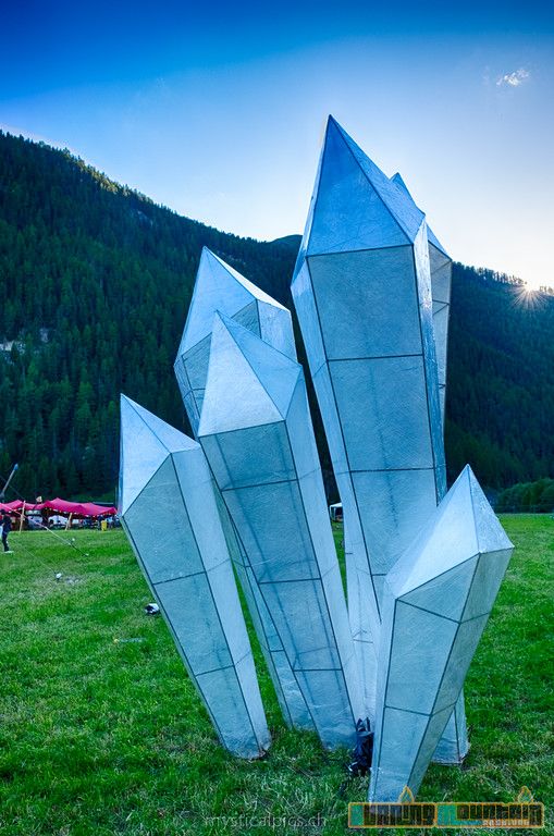 three metal sculptures in the middle of a grassy field with mountains in the background at dusk