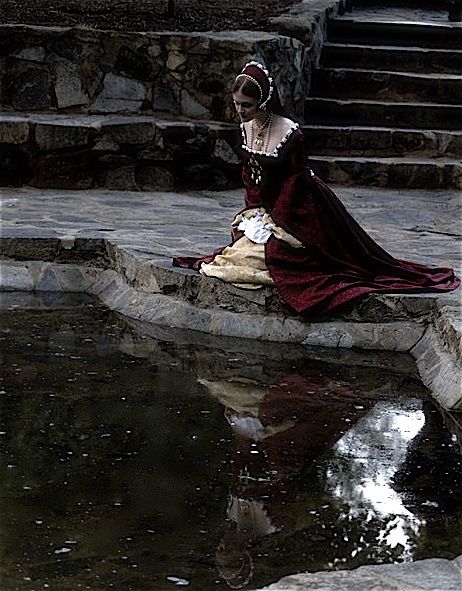 a woman sitting on steps next to a body of water wearing a long red dress