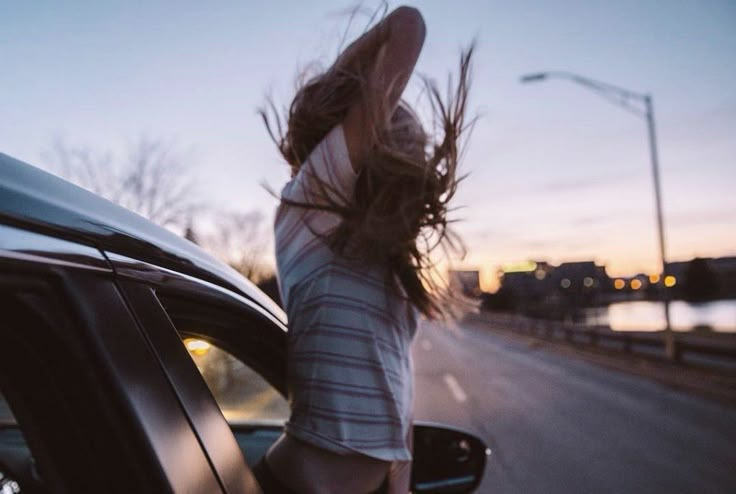 a woman leaning out the window of a car with her hair blowing in the wind