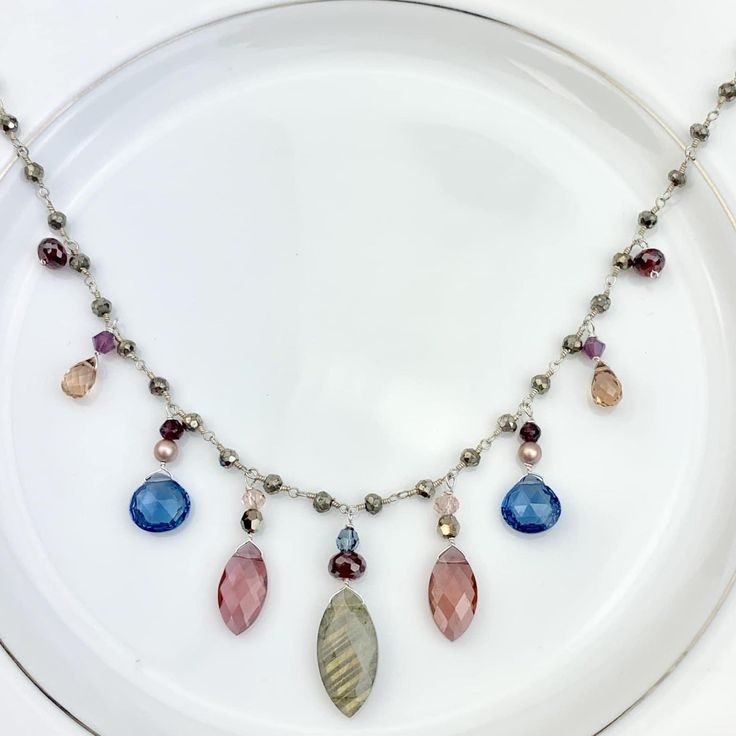 Elegant drape necklace featuring Marquee Gems as accents on Pyrite rosary style chain with draping marquee Labradorite and Marsala Qz, heart shape Spinel Qz and teardrop Dk Tea Qz. Length: 18-20″ (can request up to 24″ as well, no extra charge) Best Selling Necklace!