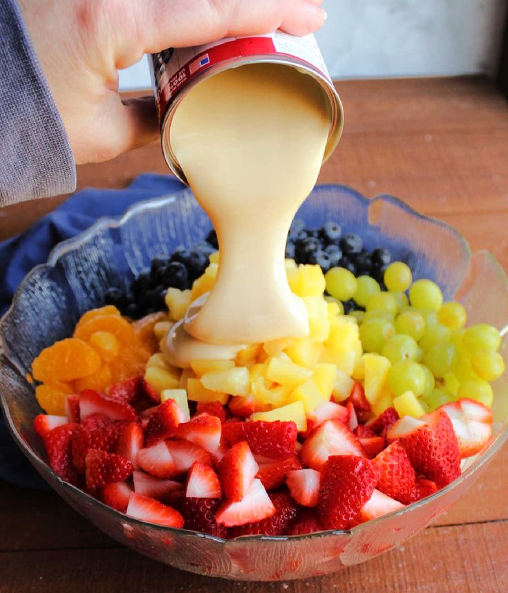 someone pouring dressing into a bowl full of fruit