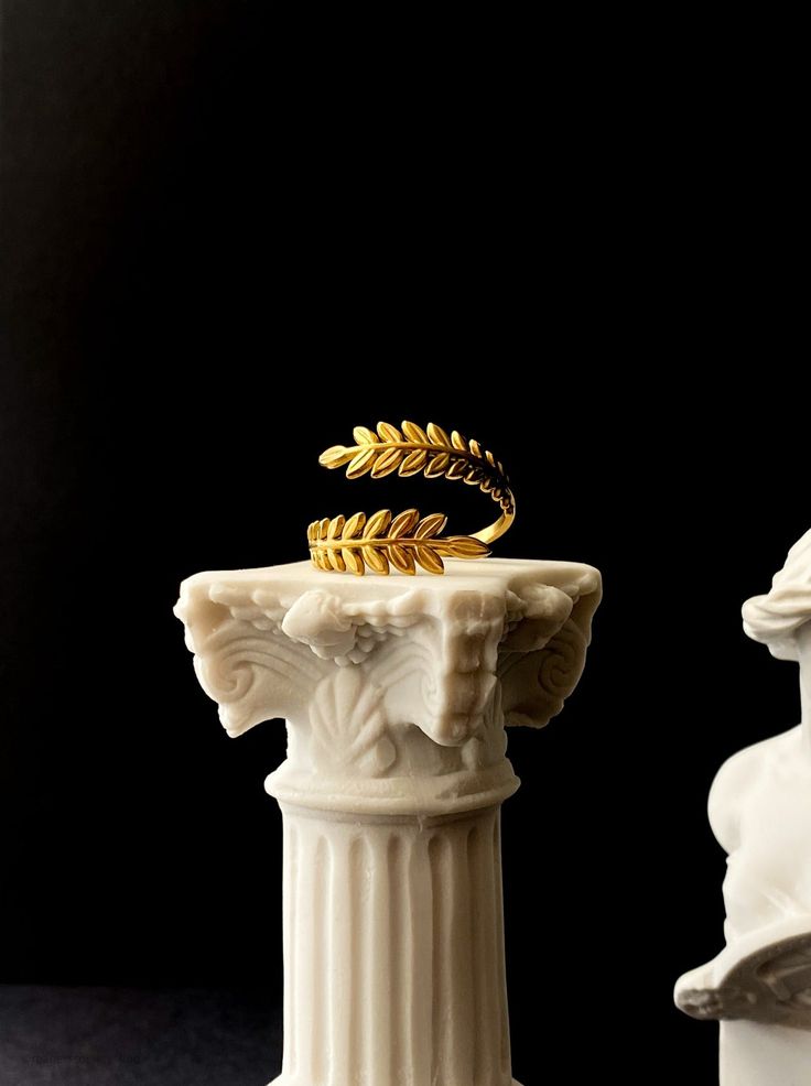 a gold ring sitting on top of a white pedestal next to another one with an ornate design