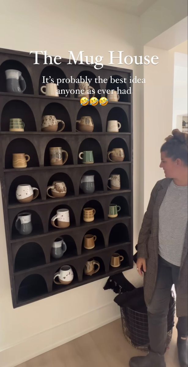 a woman standing in front of a shelf filled with cups and mugs on it