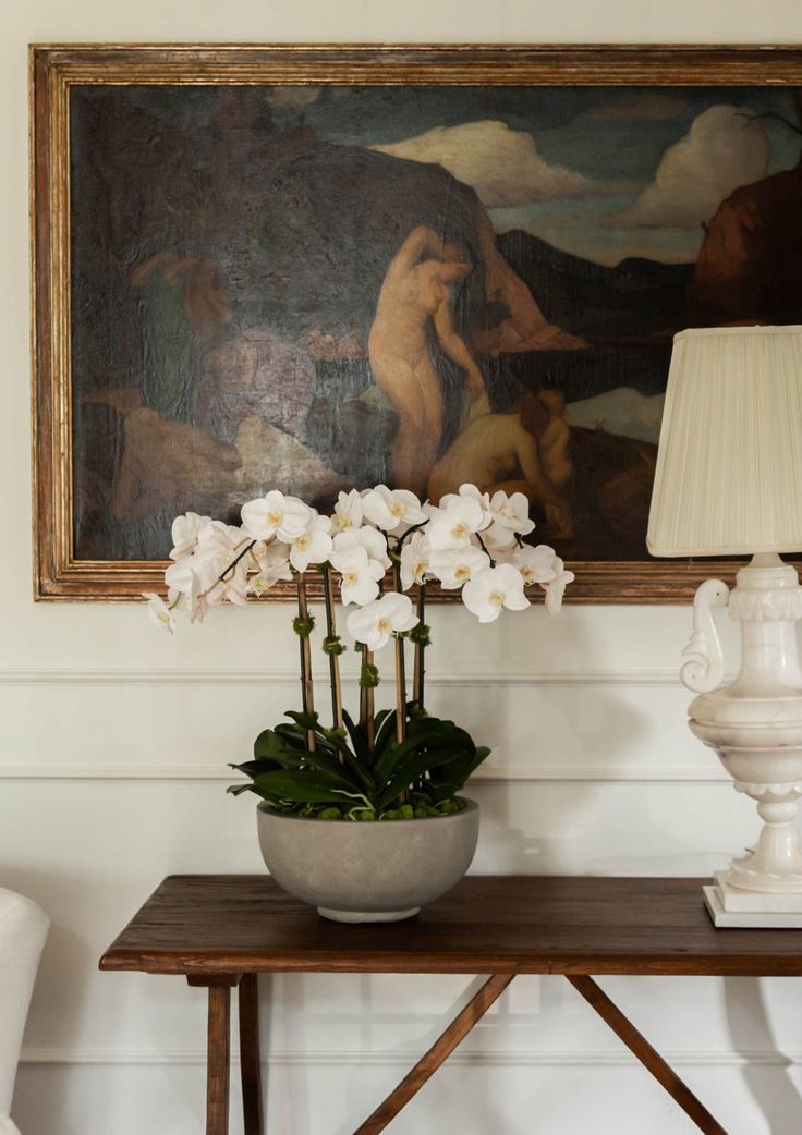 a vase with white flowers sitting on a table in front of a painting and lamp