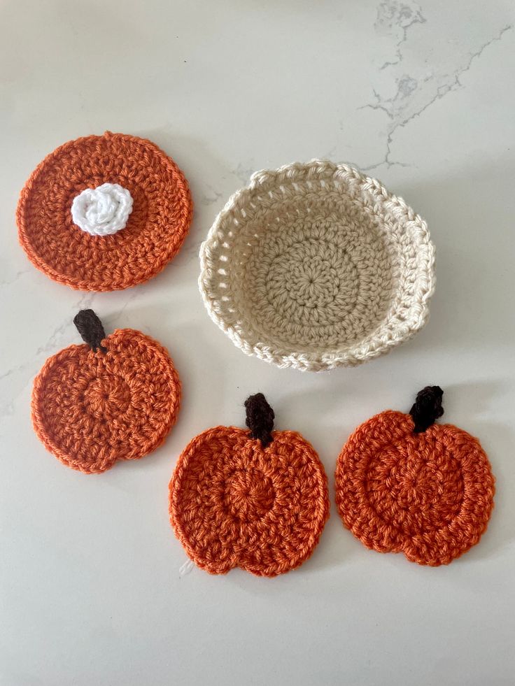 four crocheted pumpkin coasters on a white table with one orange and the other brown