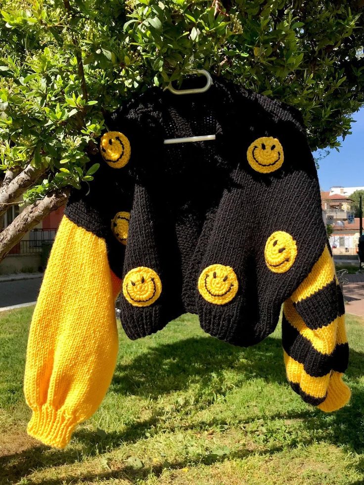 two sweaters hanging from a tree with smiley faces on them