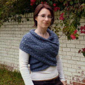 a woman standing in front of a brick wall wearing a blue knitted shawl