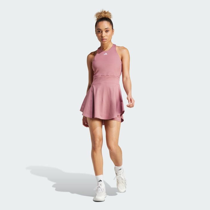 a woman in a pink tennis dress is standing on a white background and looking at the camera