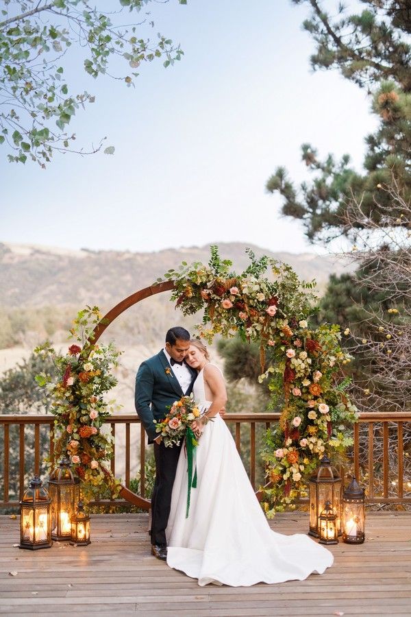 a bride and groom standing in front of an arch decorated with flowers, candles and greenery