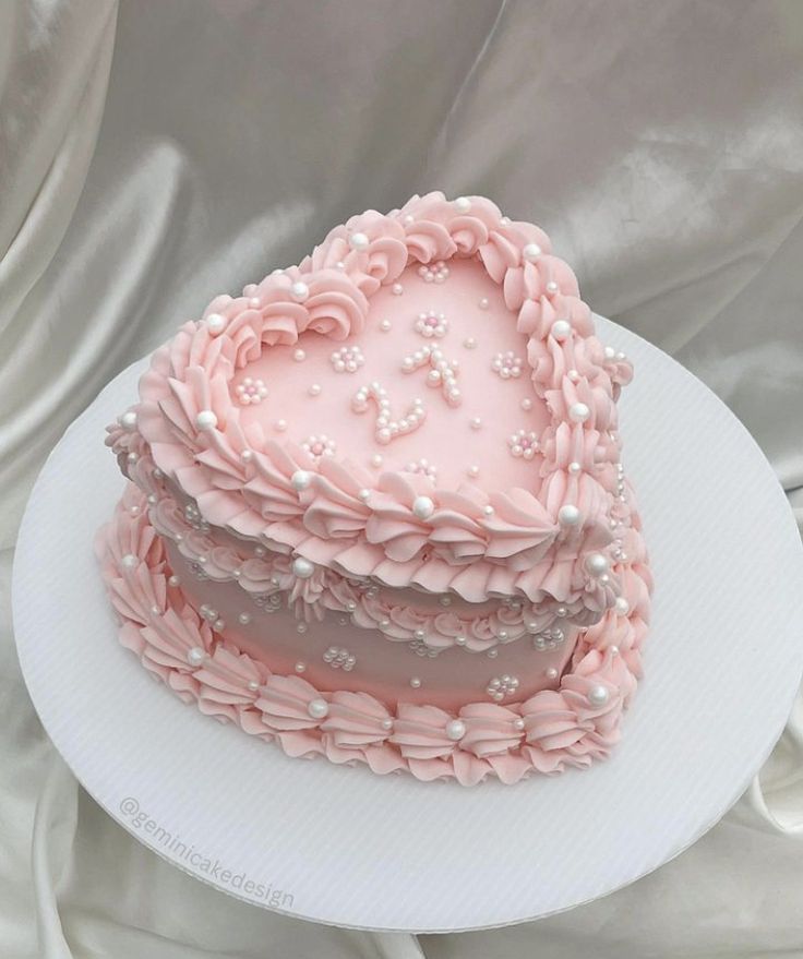 a heart shaped cake with pink frosting and pearls on top sits on a white plate