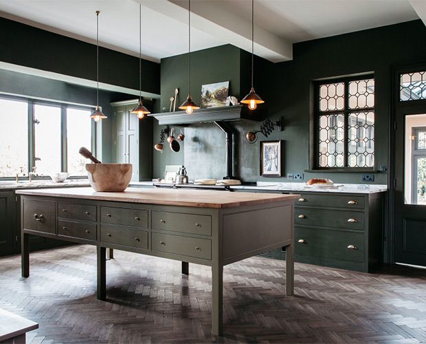 a kitchen with dark green walls and wooden floors, an island in the middle is surrounded by windows