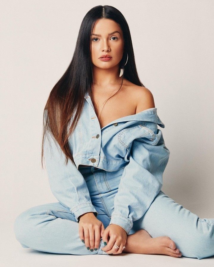 a woman sitting on the ground wearing blue jeans and looking off to the side with her hands in her pockets