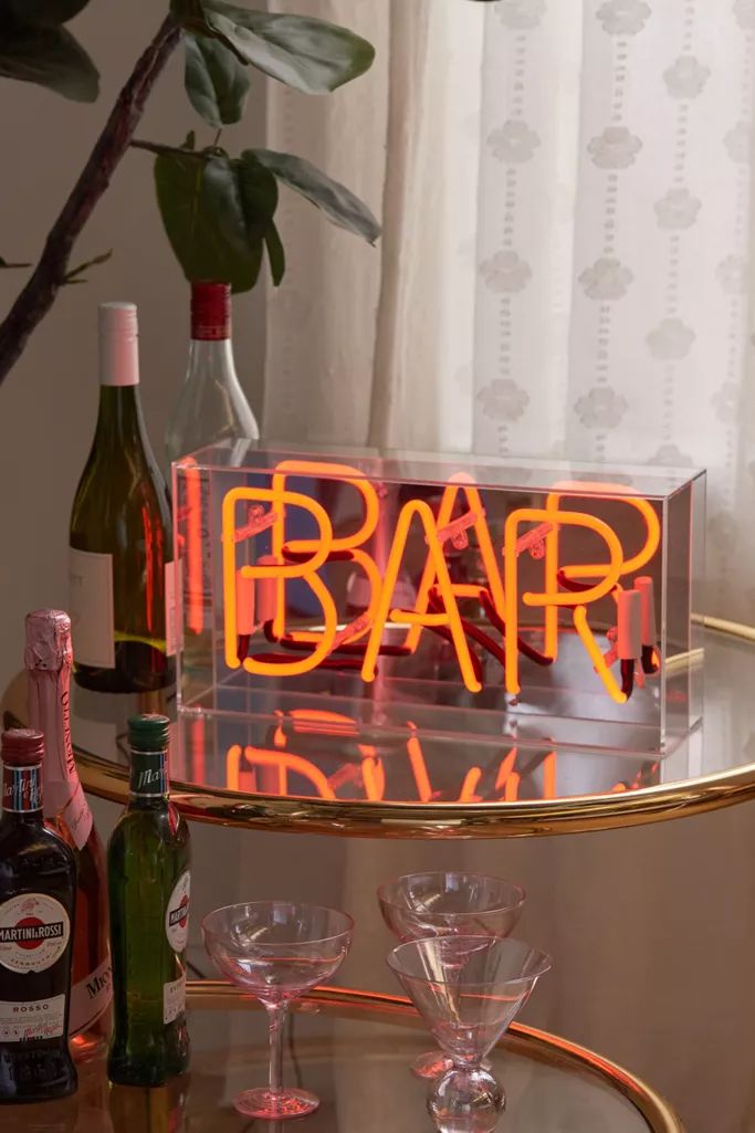 an illuminated bar sign sitting on top of a glass table next to bottles and glasses