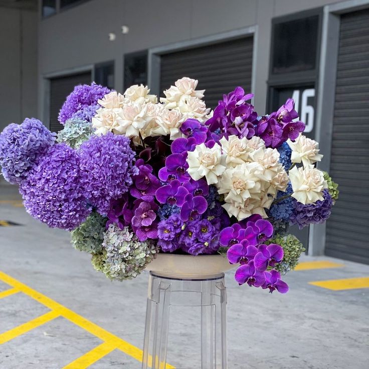 purple and white flowers sit on top of a stool in front of an industrial building